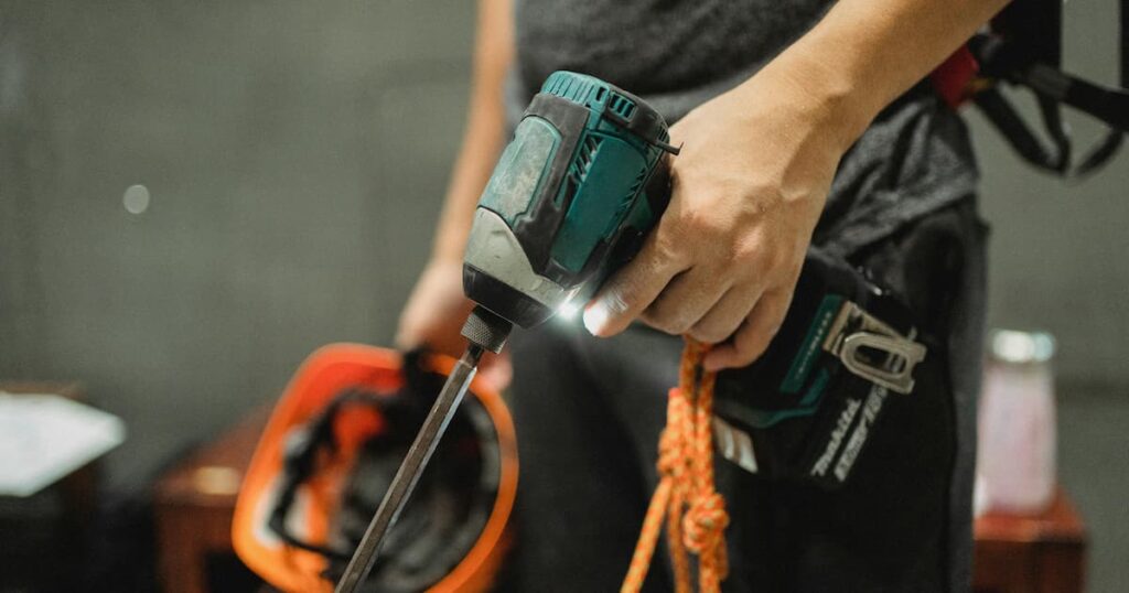 Male holding power drill and orange hard hat ready for tethering