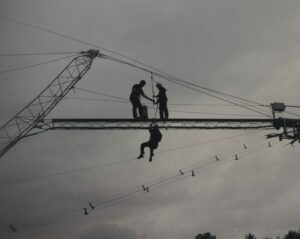 A team of construction workers engaged in a height safety training course, demonstrating the proper use of Fall Arrest and Fall Restraint Systems to lower a harnessed worker.