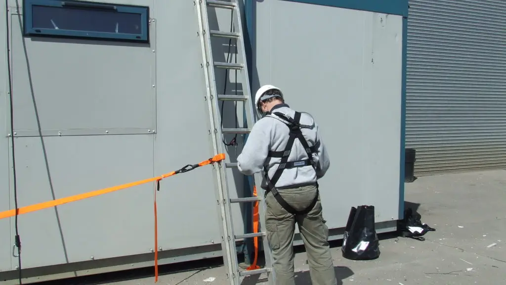 Man on ladder safety course wearing harness and safety helmet