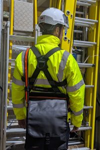 male holding tool bag wearing harness, hi-vis and hard hat